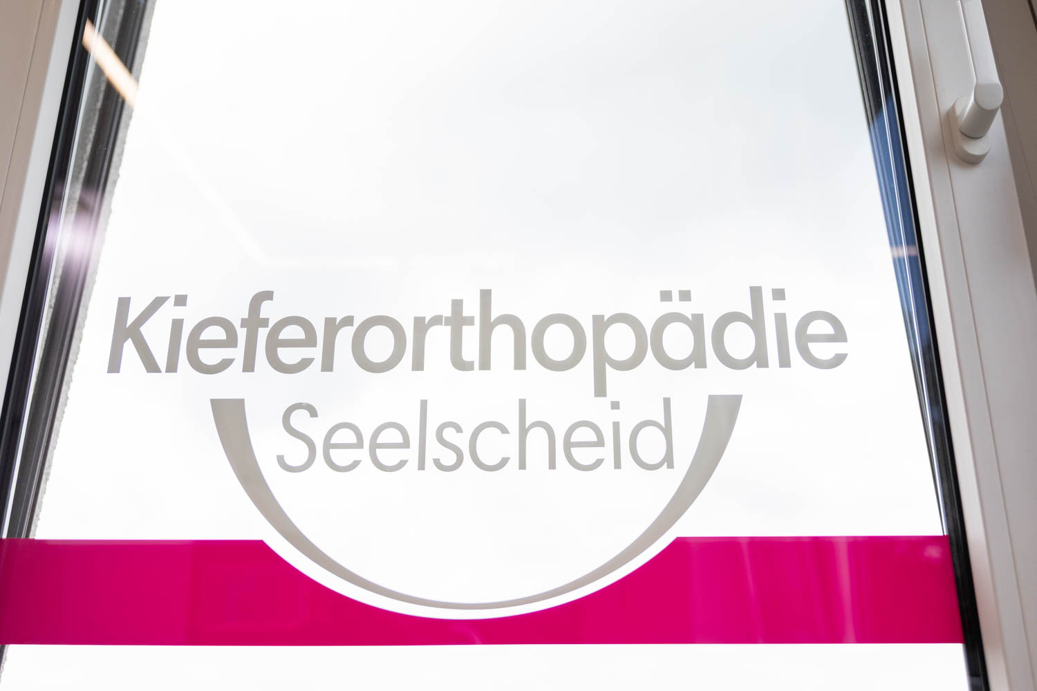 Praxislogo Kieferorthopädie Seelscheid als Folierung auf einer Fensterscheibe der Fachpraxis in Neunkirchen-Seelscheid.