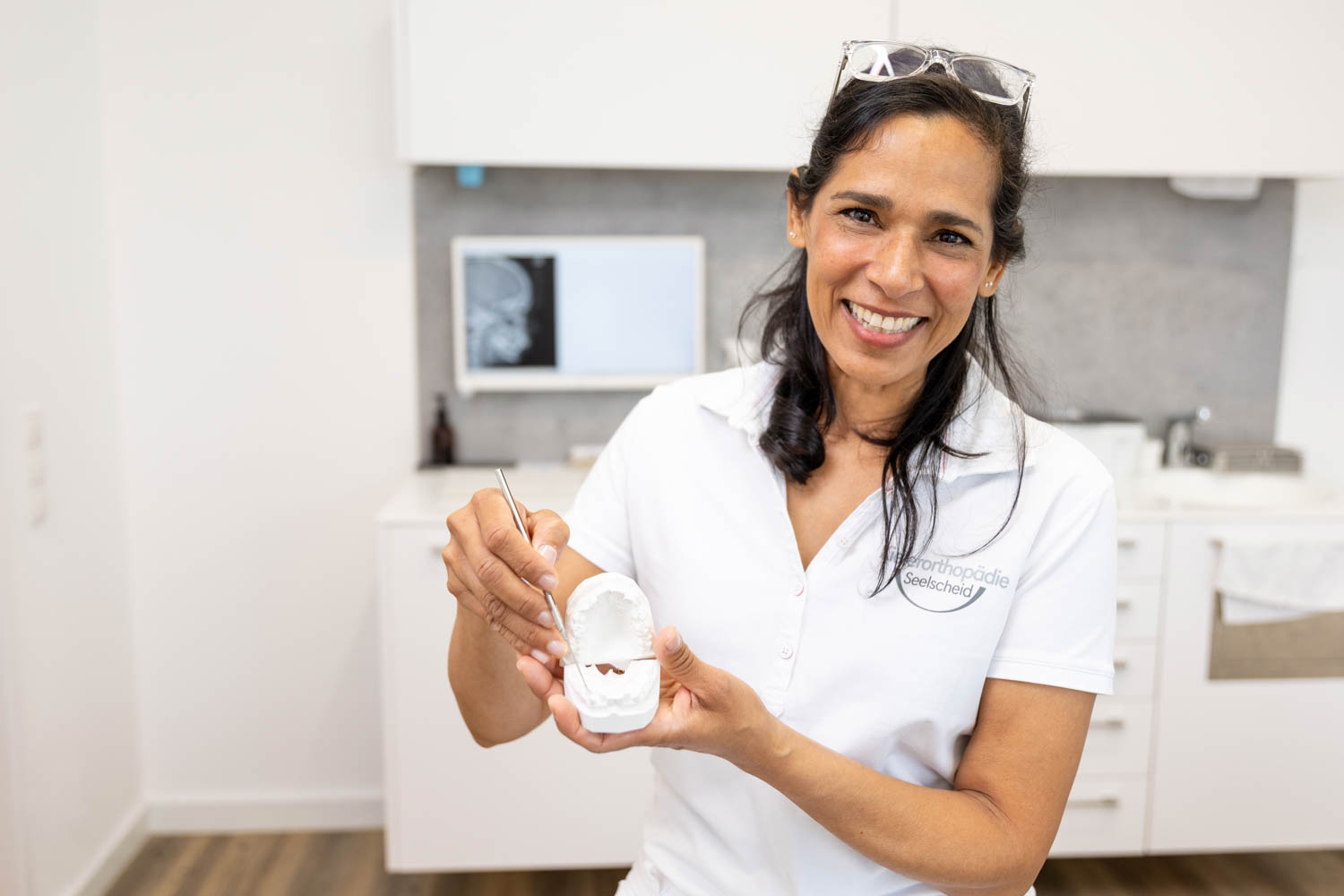 Kieferorthopädin Dr. Garcia lächelt freundlich und hält ein weißes Gipsmodell eines Gebisses sowie ein Behandlungsinstrument in der Praxis Kieferorthopädie Seelscheid in Neunkirchen-Seelscheid.