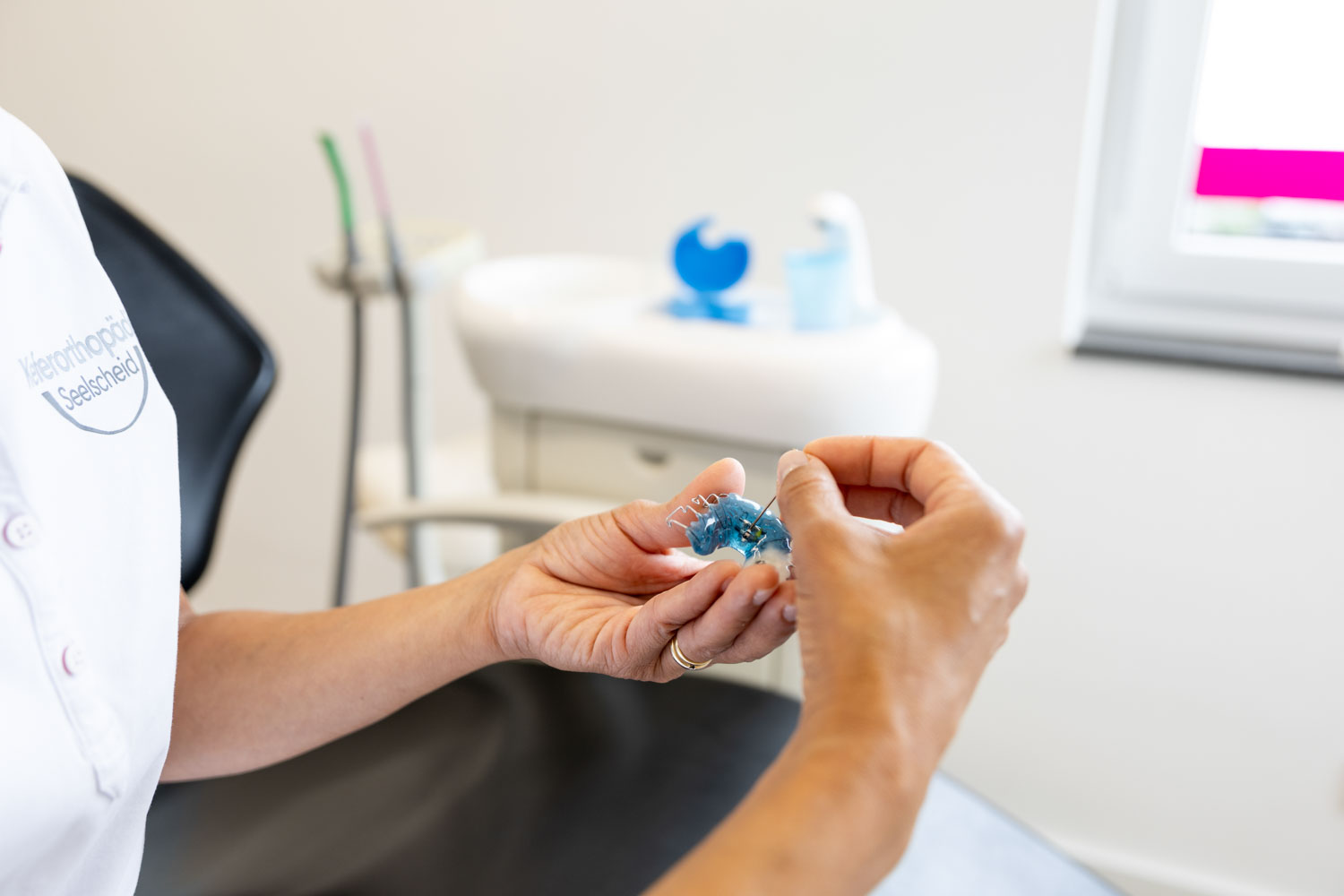 Eine Mitarbeiterin stellt mit einem kleinen Spezialschlüssel eine herausnehmbare blaue Zahnspange in der Praxis Kieferorthopädie Seelscheid in Neunkirchen-Seelscheid ein.